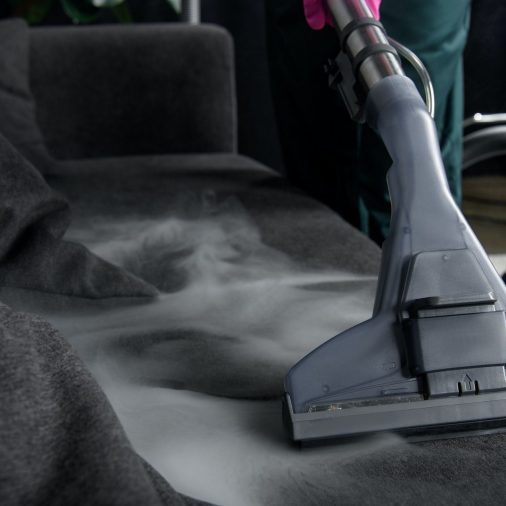 close-up view of person cleaning sofa with vacuum cleaner, hot steam cleaning concept